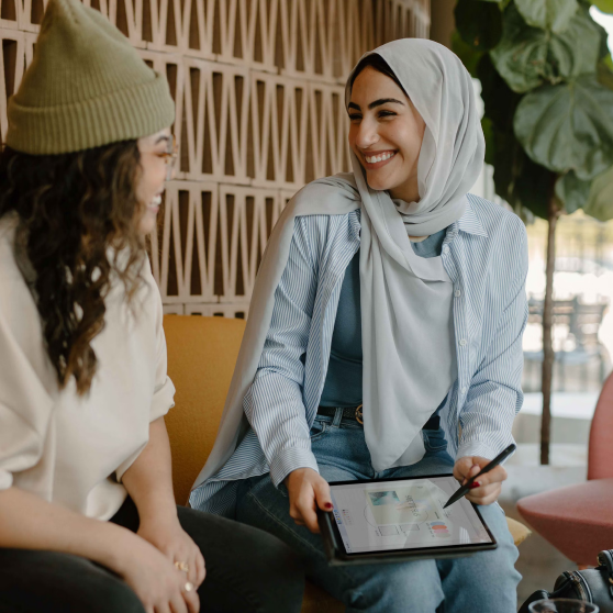 Two women laughing. One holding a tab